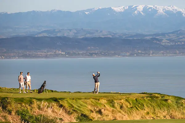 A golfer strikes a tee shot on a beautiful golf course by the sea