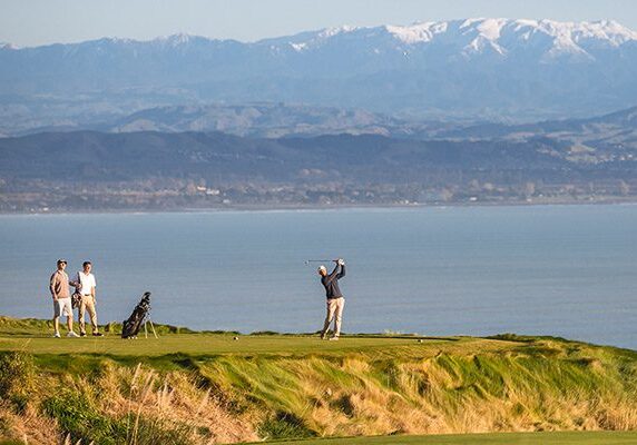 A golfer strikes a tee shot on a beautiful golf course by the sea